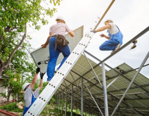 Installing of stand-alone solar photo voltaic panel system. Team of three technicians mounting big shiny solar module on high metal platform. Alternative energy and professional construction concept.